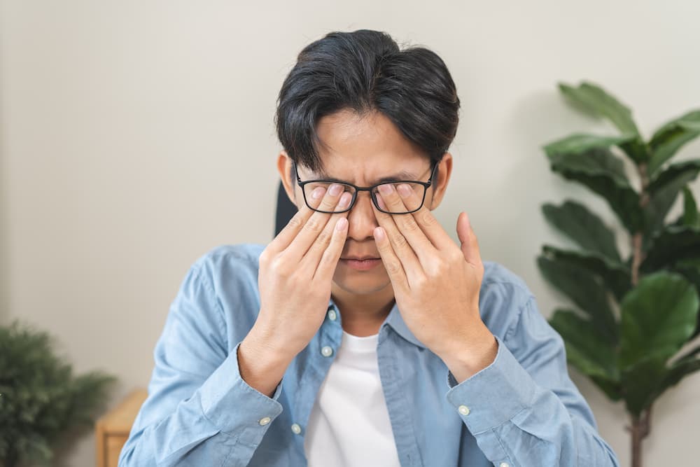 Mann mit Brille reibt sich die Augen im Büro wegen trockenen Augen